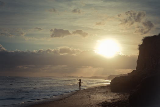 A lone figure stands on a tranquil beach, silhouetted against a vibrant sunrise over the ocean.