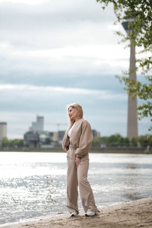 A woman standing on the shoreline in a beige outfit