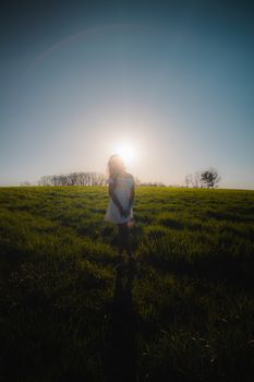 A woman in a white dress stands silhouetted against the setting sun in a grassy meadow, Mansfield, CT.