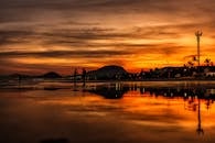 日落时分，渔民剪影倒映在宁静的湖面上，与山脉相映成趣