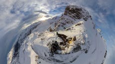 冬日天空下，一名登山者在白雪皑皑的山峰上休息，景色迷人