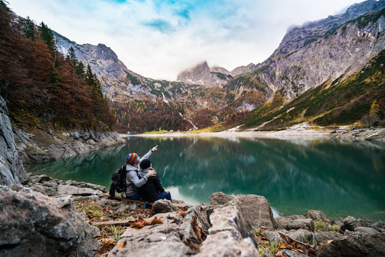 Couple Sitting On Rock Beside Lake