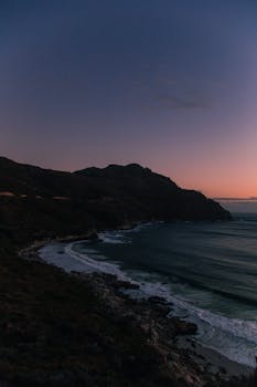 在南非崎岖的海岸线上，壮丽的日落映照着宁静的海浪和雄伟的山脉
