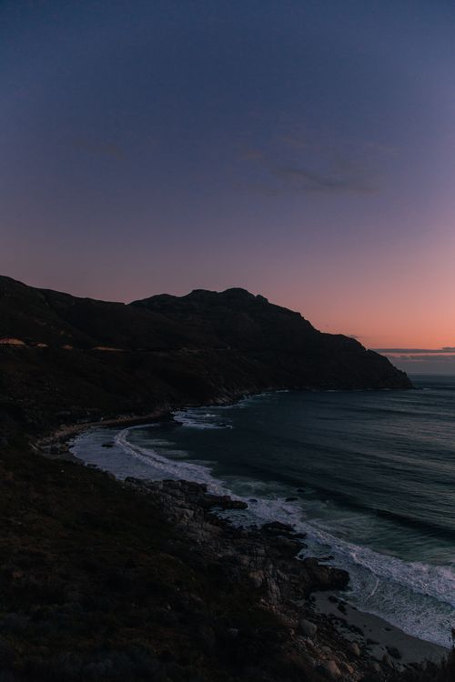 Free A stunning sunset over the rugged coastline in South Africa, capturing serene ocean waves and majestic mountains. Stock Photo