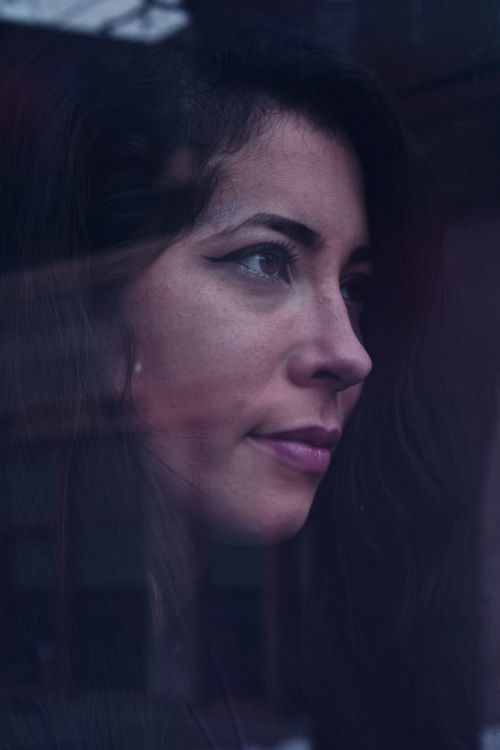 Free A thoughtful portrait of a woman gazing reflectively through a window, captured in natural light. Stock Photo