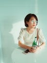 一位戴着眼镜的亚洲女性坐在明亮的室内，身旁是一张摆着啤酒瓶的桌子