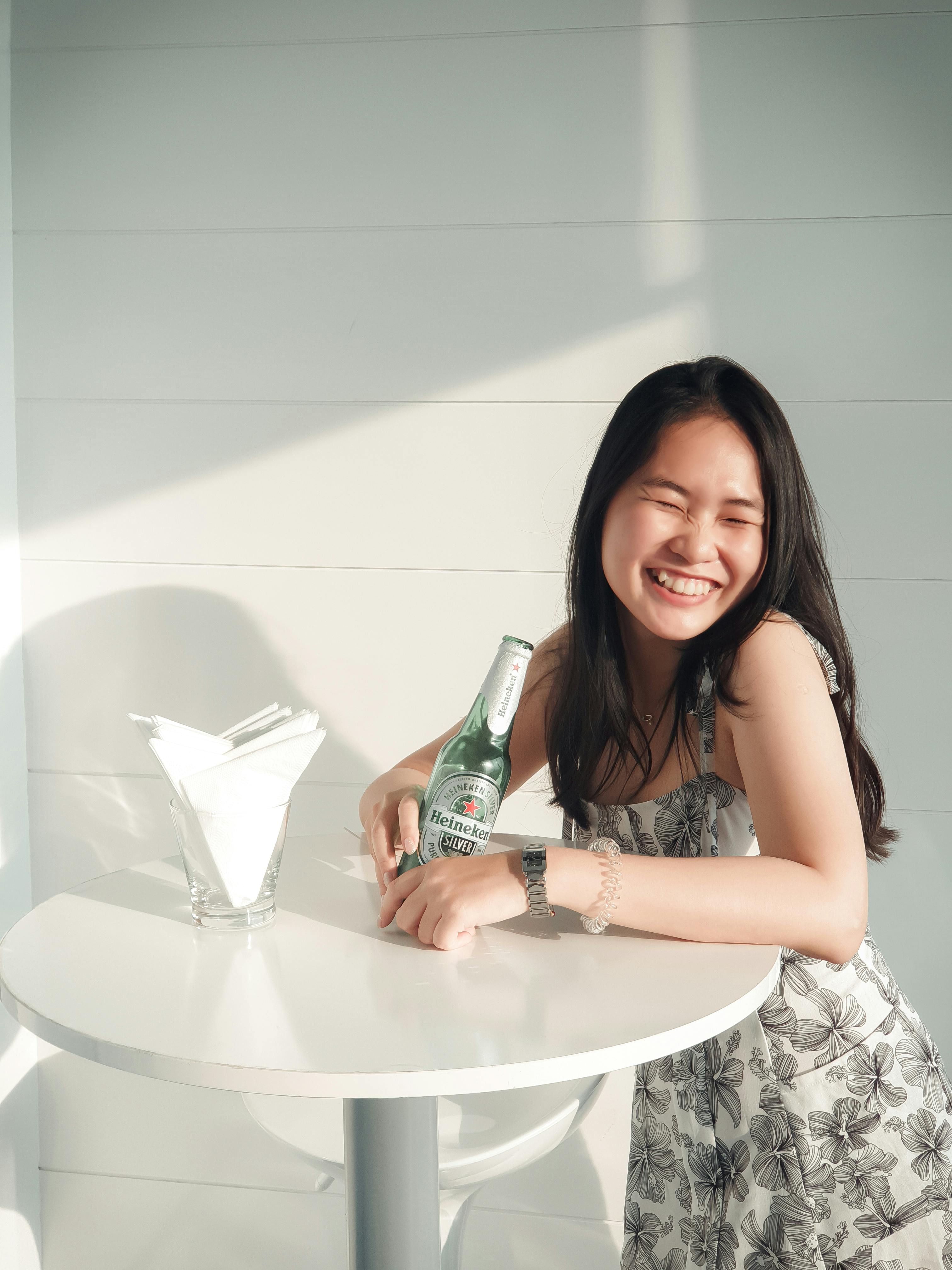 smiling woman standing beside table while holding heineken beer bottle