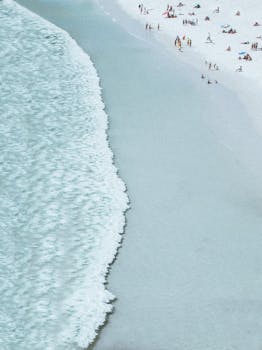 从空中俯瞰，沙滩上浪花轻柔，人们在夏日里享受着日光浴