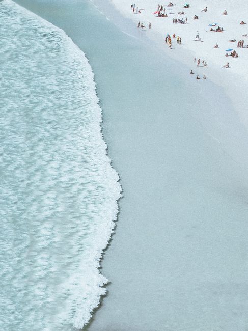 Aerial shot of a sandy beach with gentle waves and people sunbathing on a summer day.