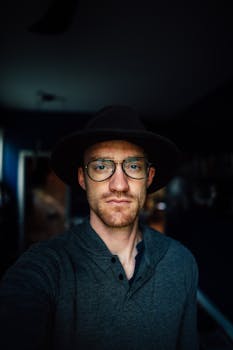 一位戴着眼镜和帽子的时尚男士，在室内自信地摆着姿势