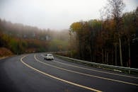 一辆汽车穿过薄雾笼罩的秋日森林，在道路上行驶，突显了自然与旅行的意境