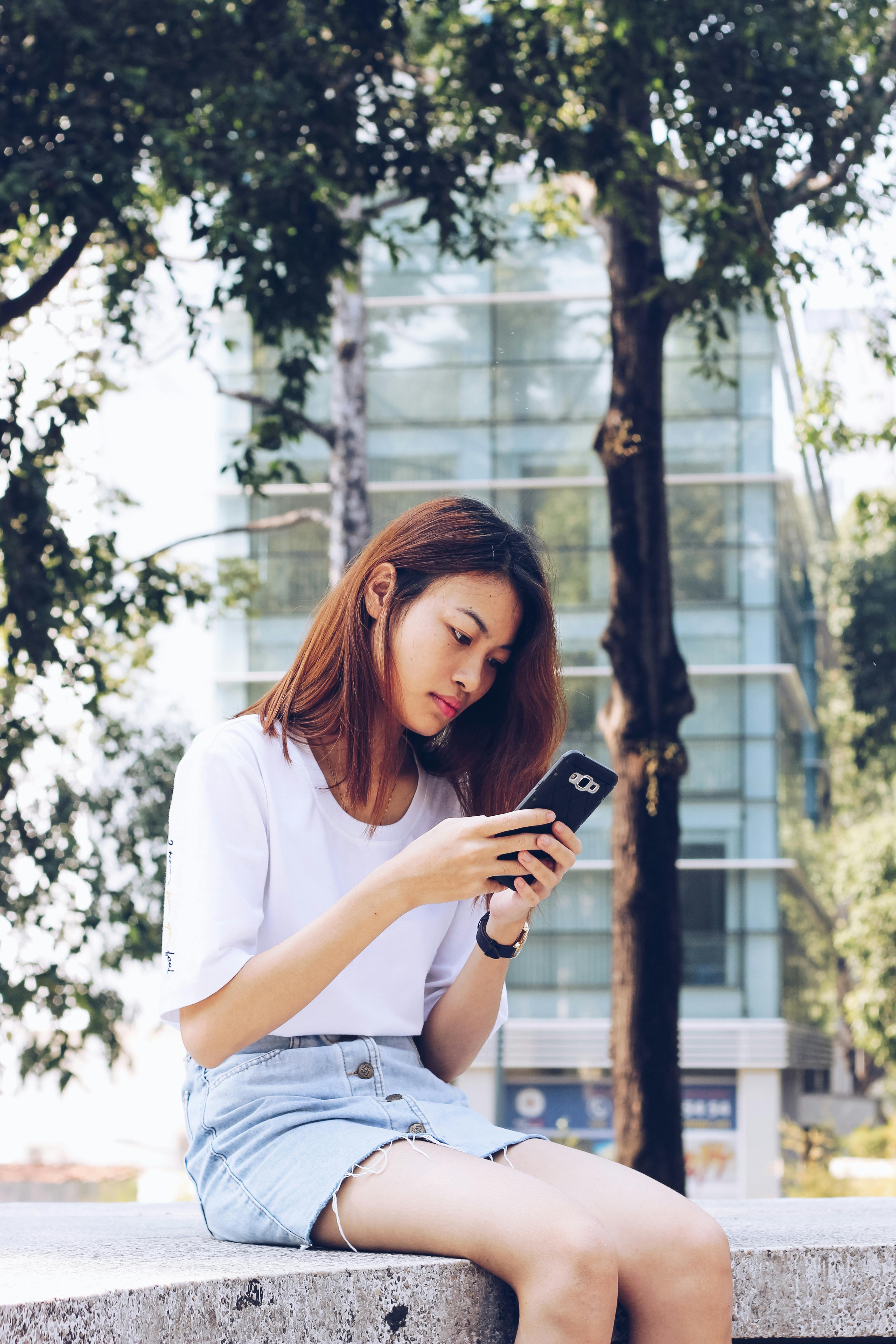 Woman Using Her Phone While Sitting on Concrete Bench