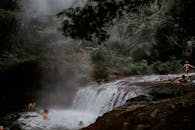 一群人享受着天然瀑布，周围薄雾缭绕，雨林茂密