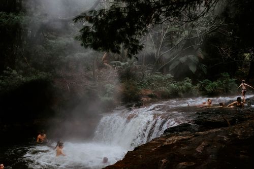Free A group of people enjoying a natural waterfall surrounded by mist and lush rainforest environment. Stock Photo