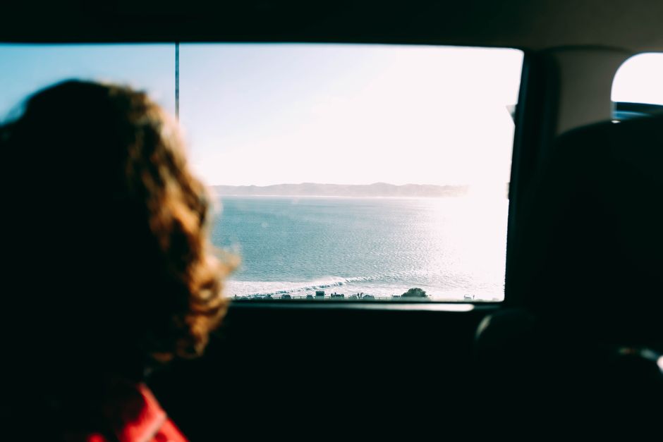 Woman enjoys scenic coastal view from car window, capturing serene travel moments.