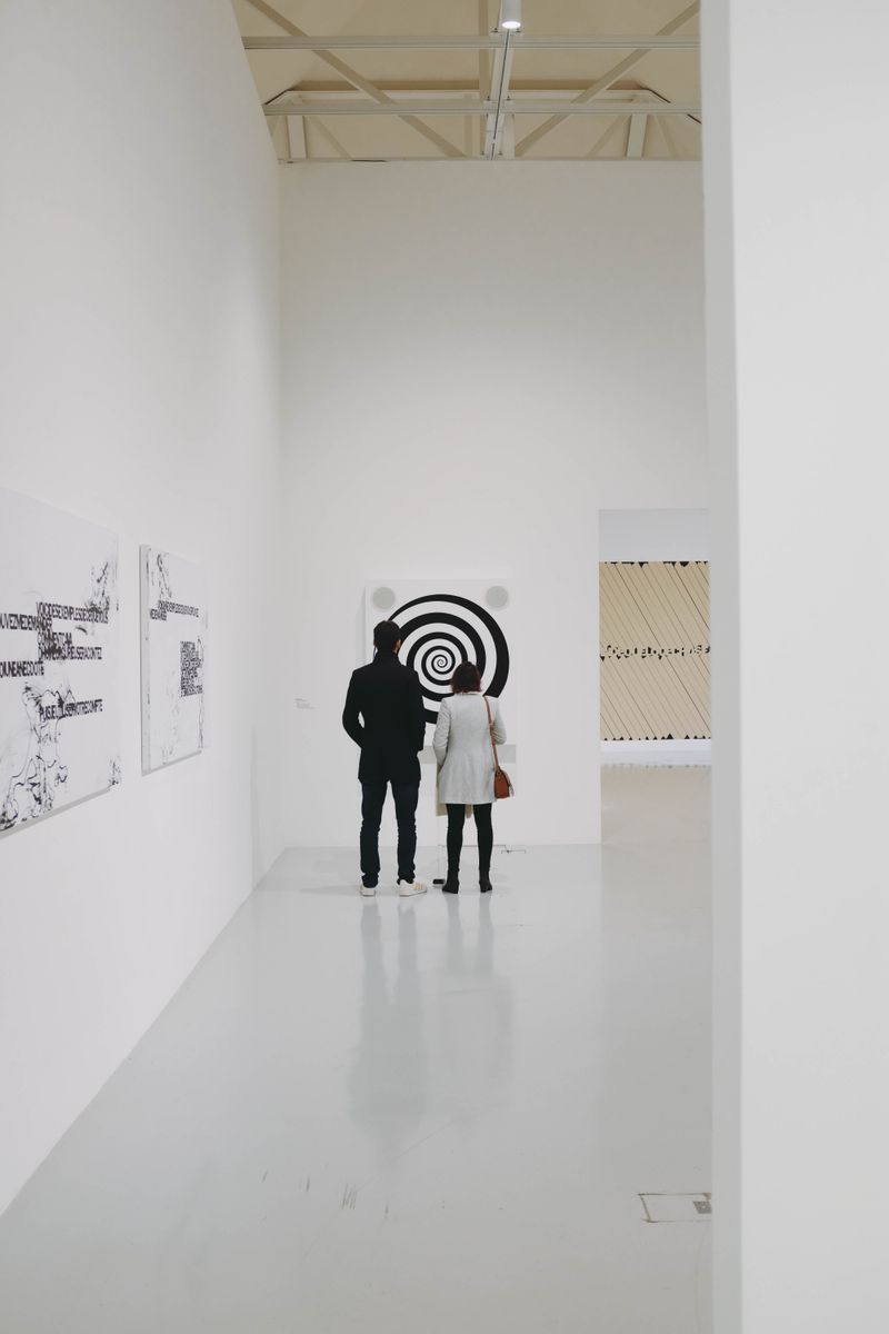 Two visitors in a white-walled exhibition room — Adrien Olichon on Pexels