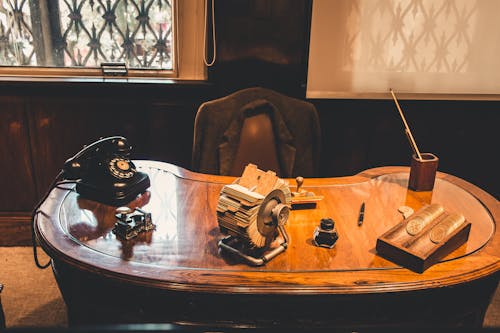 Black Rotary Telephone and Coin Collection on Top of Brown Table