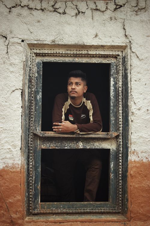 Free A contemplative man gazes outside through a rustic window frame in a textured wall. Stock Photo