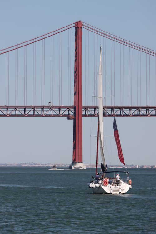 Free A sailboat passes beneath the iconic 25 de Abril Bridge in Lisbon, Portugal. Stock Photo