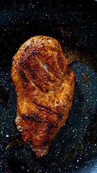 Close-up of a seasoned grilled chicken breast on a dark frying pan surface.