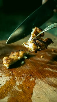 Juicy grilled chicken piece being cut on a rustic wooden board with a knife and fork.