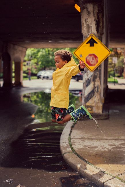 Happy child in a yellow raincoat joyfully jumping in a puddle by a street sign on a rainy day.