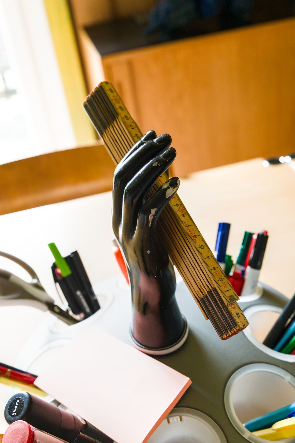 A hand-shaped pen holder gripping a ruler among pens and markers