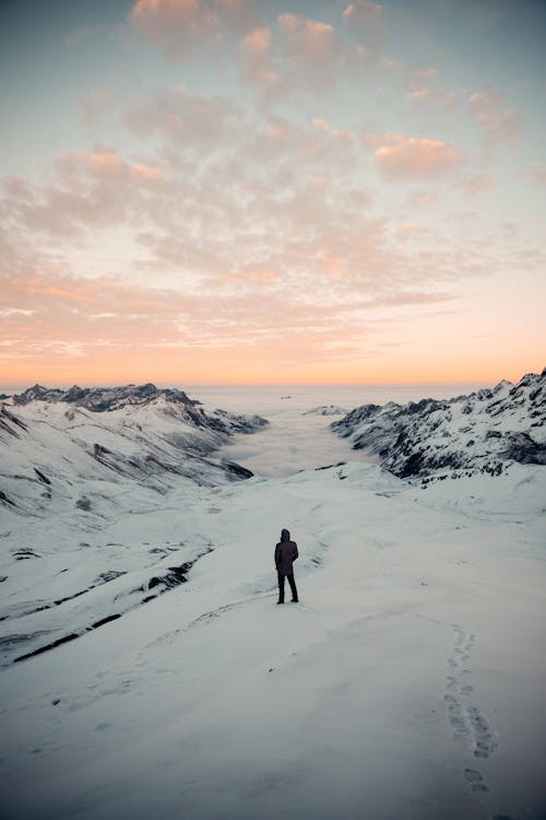 Person Standing in Snowy Field Under White and Orange Skies