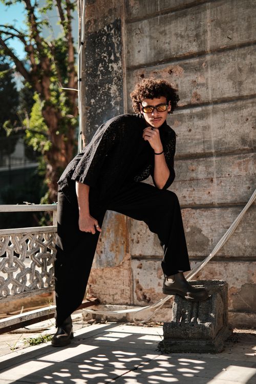 Free Model posing in urban setting wearing fashionable black outfit and eyeglasses, leaning on wall. Stock Photo
