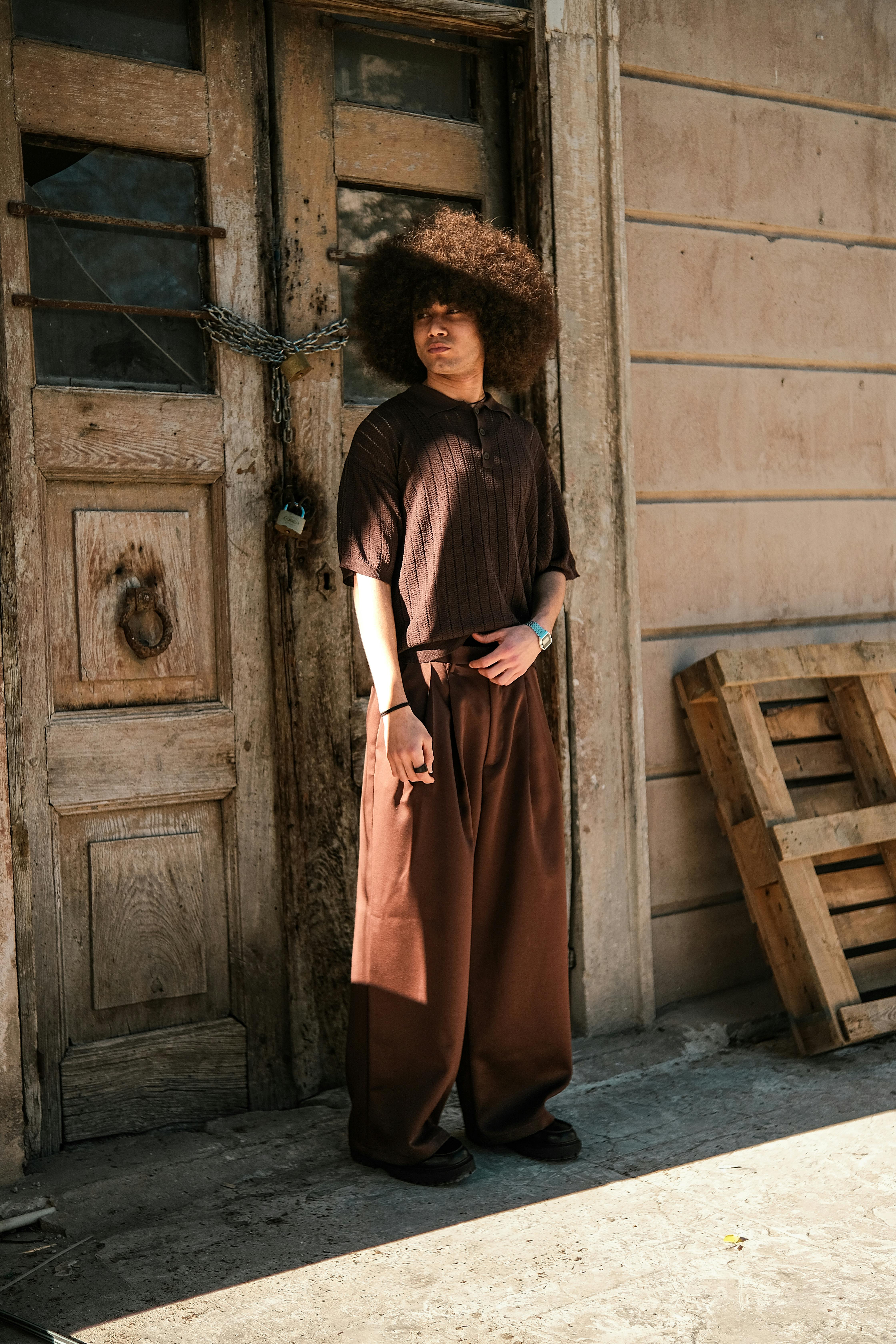 Model with afro hairstyle posing in urban setting by a rustic door.
