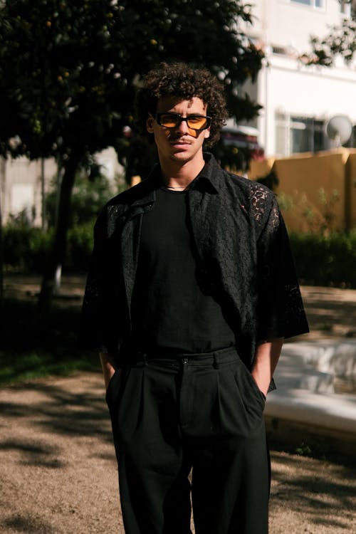 A man in sunglasses and black shirt standing in a park