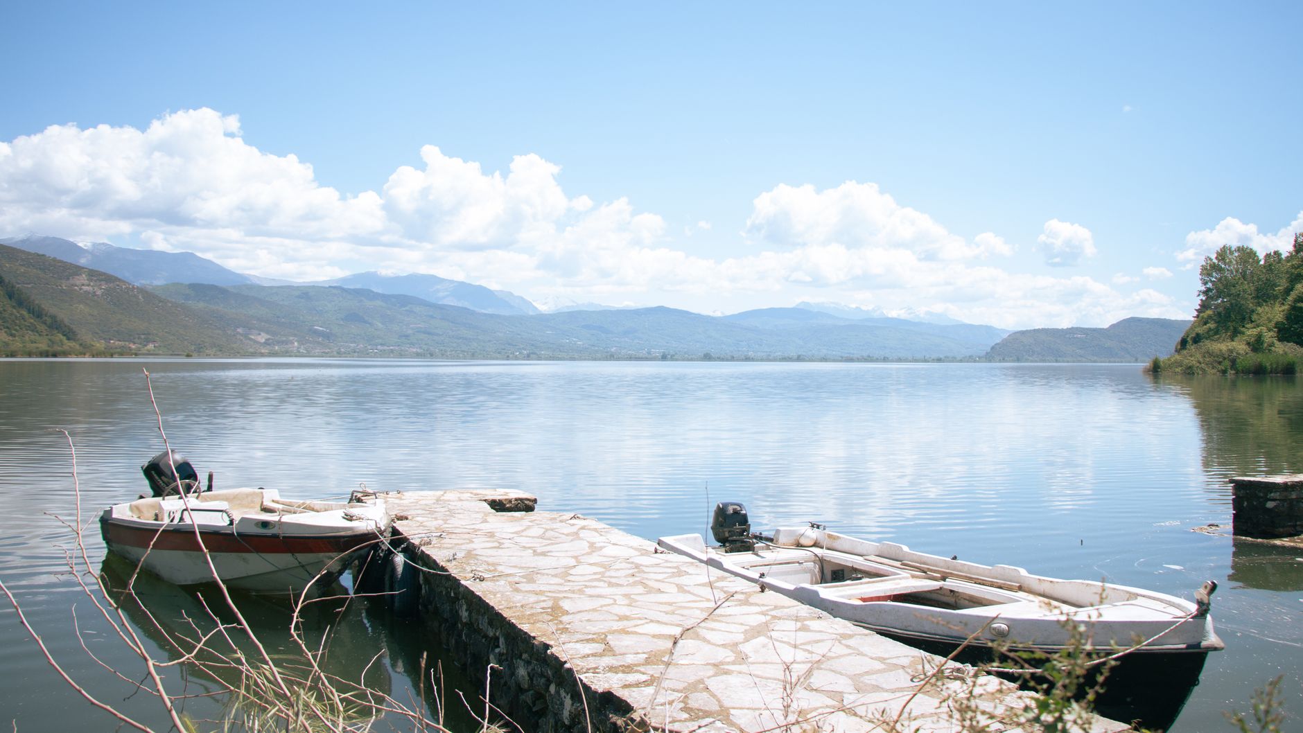 Serene view of motorboats moored on Lake Ioannina's pier with mountain backdrop.