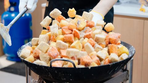 Vendor frying colorful tofu cubes at an Asian market stall. Captured in an urban setting, showcasing vibrant street food culture.