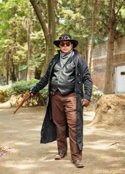 A steampunk enthusiast poses in a forest wearing vintage attire and accessories.