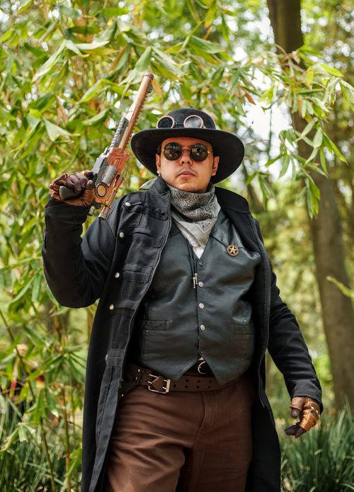 Free A man in steampunk attire poses with a gun in a lush park. Stock Photo