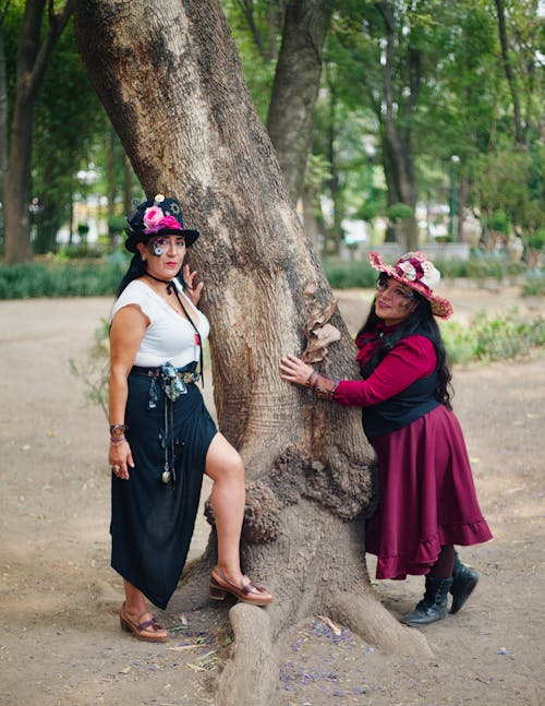 Two women in hats posing near a tree