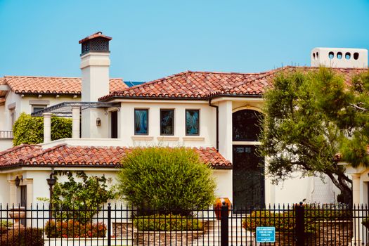 Beautiful two-story Mediterranean-style house with lush greenery and wrought iron fence.