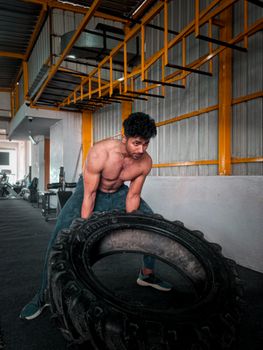 A muscular man exercising by lifting a large tire in a modern gym setting.