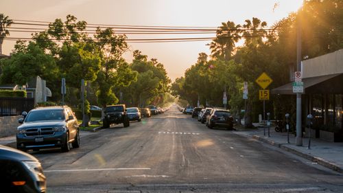 Free Sunset view of a tranquil urban street with parked cars and lush green trees. Stock Photo