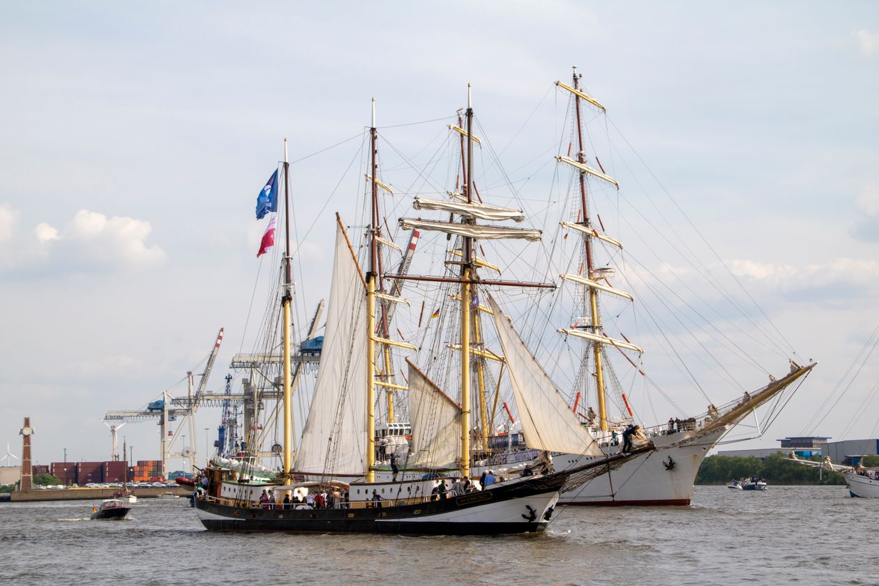 Tall sailing ships with large white sails moored side by side in a port harbour before a grand sailing festival