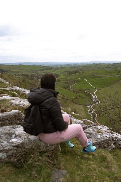 A woman sitting on a rock looking out over a valley