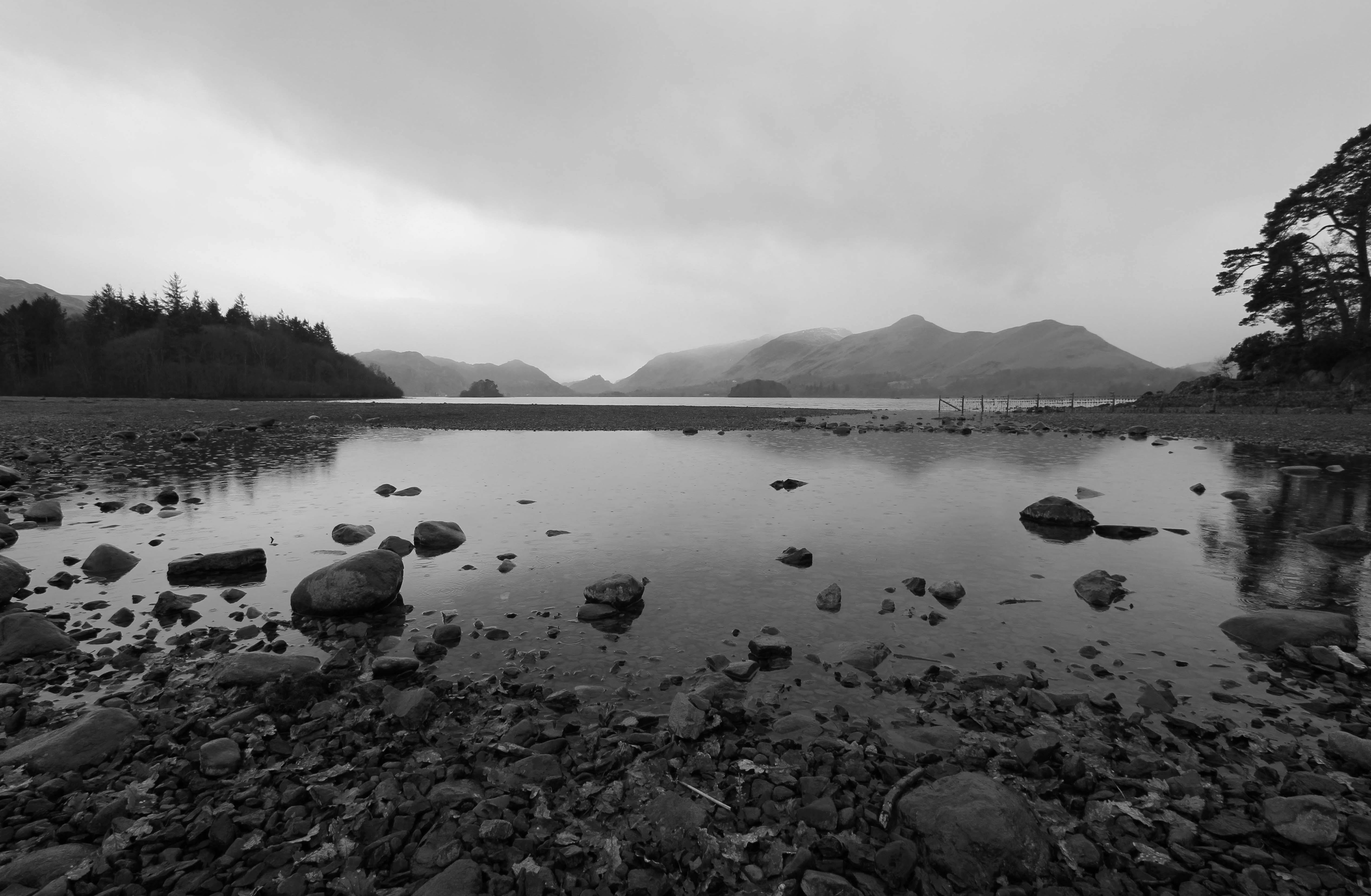 A serene black and white landscape of Derwentwater in Keswick, featuring mountains and rocky shores.