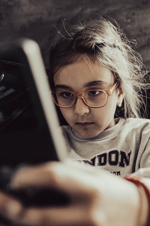 A young girl wearing glasses is looking at a tablet