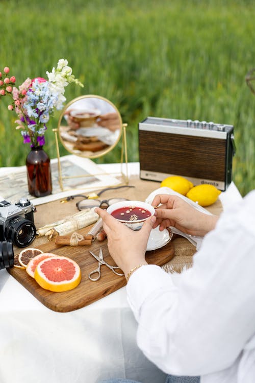 A woman sitting on a picnic table with a camera and a glass of juice