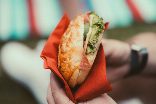 Hand holding a delicious sandwich with cheese, salami, and lettuce wrapped in a red napkin.