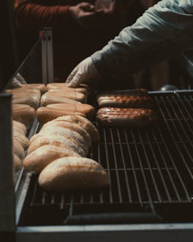 Close-up of grilling sausages and buns, showcasing food preparation at an outdoor barbecue.