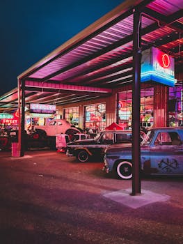 Classic cars parked at a neon-illuminated retro garage during evening. Urban vintage vibe.
