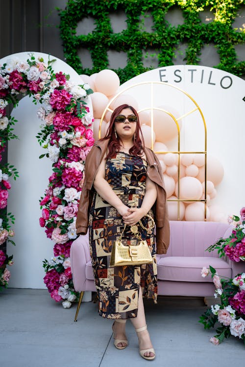 A woman in a floral dress and sunglasses poses for a photo