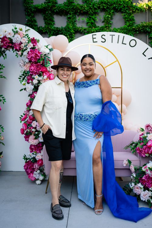 Free Two smiling women pose in stylish outfits at a chic fashion event featuring vibrant floral decorations. Stock Photo