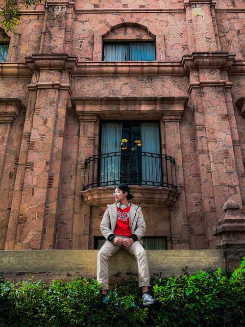 Free Young man in casual fashion sits on ledge, historic stone facade background. Stock Photo